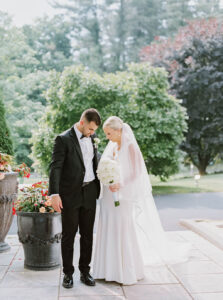 The couple stands together near the entrance with lush greenery behind them, holding hands in a calm moment that reflects the natural flow of a Wadsworth Mansion CT wedding.