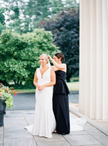 A bridesmaid adjusts the bride’s veil beneath tall white columns, capturing a quiet preparation moment typical of a Wadsworth Mansion CT wedding.
