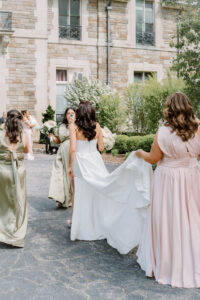 Bride walking with her bridesmaids outside a stone estate while her veil trails behind her at a luxury wedding venue in Newport RI.