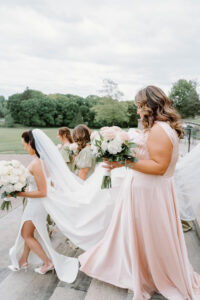 Bridesmaids helping arrange the bride’s veil before the ceremony with sweeping lawn views and coastal light at a Newport mansion wedding venue.