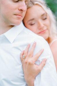 Harkness Park Wedding | Deirdre Photography Timeless and Organic Moments | A woman with long blonde hair gently embraces a man from behind, eyes closed and smiling. Her hand rests on his shoulder, displaying an engagement ring.