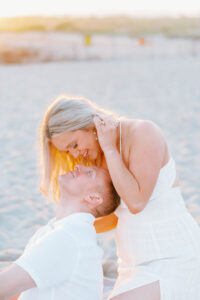 Harkness Park Wedding | Deirdre Photography Timeless and Organic Moments | A couple in white embraces on a sunlit beach, sharing a tender moment. The warm glow of sunset creates a serene and romantic atmosphere.
