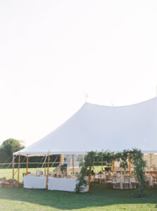 Eisenhower House Wedding | Deirdre Photography Timeless and Organic Moments | A large white tent stands on green grass under a clear sky, with wooden poles and greenery accents. Inside, tables are set for an outdoor gathering.