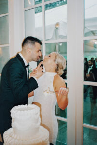 Indoors, the bride and groom share a playful kiss while cutting their cake, highlighting a candid reception moment from a Wadsworth Mansion wedding.