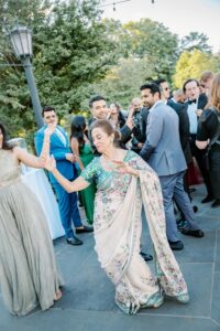 Brooklyn Botanic Garden Wedding | Deirdre Photography Timeless and Organic Moments | A joyful outdoor gathering with people in formal wear dancing. An elder woman in a floral sari dances with a younger woman in a shimmery gown.