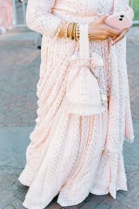 Brooklyn Botanic Garden Wedding | Deirdre Photography Timeless and Organic Moments | Woman wearing an ornate pink embroidered lehenga with gold bangles holds a smartphone. A matching pink embellished purse hangs by her side.