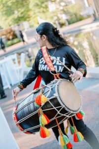 Brooklyn Botanic Garden Wedding | Deirdre Photography Timeless and Organic Moments | A person wearing a black shirt plays a colorful dhol drum outdoors. The drum features vibrant tassels.