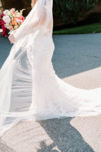 Wedding Photographers Newport RI | Deirdre Photography Timeless and Organic Moments | Bride in a flowing white gown and veil walking outdoors, holding a colorful bouquet of flowers. Sunlight casts soft shadows