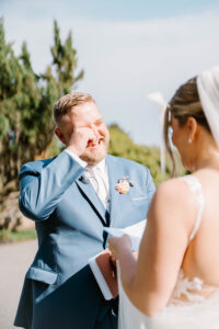 Wedding Photographers Newport RI | Deirdre Photography Timeless and Organic Moments | A groom in a blue suit wipes a tear while facing the bride during an outdoor ceremony.