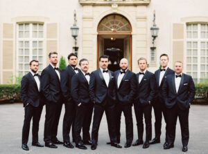 Groom and groomsmen posing in black tuxedos outside the stately entrance of one of the most iconic historic wedding venues in Rhode Island.