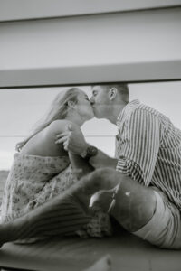 Wedding Photographer Newport Rhode Island | Deirdre Photography Timeless and Organic Moments | A couple shares a tender kiss seated on a boat, with a serene sea background. The woman wears a floral dress, and the man sports a striped shirt