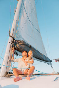 Wedding Photographer Newport Rhode Island | Deirdre Photography Timeless and Organic Moments | Couple sitting on a sailboat, embracing under the sun. With sails and blue sky in the background