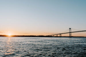 Wedding Photographer Newport Rhode Island | Deirdre Photography Timeless and Organic Moments | Sunset over a calm sea with an arching bridge stretching across the horizon. The sky transitions from orange to blue