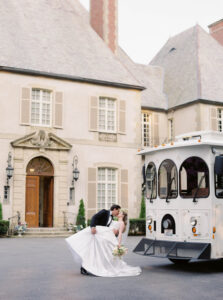 Newlyweds sharing a dip kiss beside the trolley outside the manor with elegant stonework and refined coastal charm at a Glen Manor House wedding.