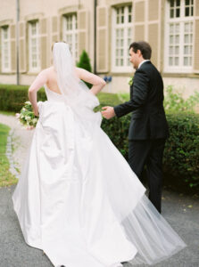 Bride and groom walking hand in hand through the estate courtyard with flowing veil and classic architecture during timeless Glen Manor House wedding photos.