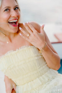 Engagement Photos Rhode Island | Deirdre Photography Timeless and Organic Moments | A smiling woman in a strapless, ruffled, light yellow dress shows off a ring.