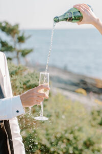 Champagne being poured beside ocean views during cocktail hour at a waterfront celebration photographed with a relaxed and elevated wedding photography RI approach.