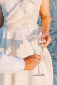 Couple holding champagne glasses beside the water during sunset cocktail hour at a waterfront wedding venue in Newport Rhode Island.