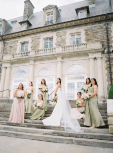 Aldrich Mansion Wedding Photos | Deirdre Photography Timeless and Organic Moments | A bride in a white gown stands on stone steps with six bridesmaids in green and pink dresses, holding bouquets, in front of a stately stone mansion.