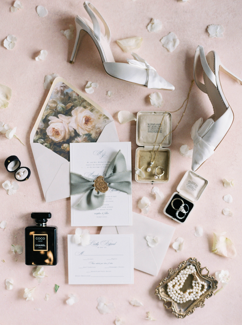 Bridal heels, invitations, rings, perfume, pearls, and floral stationery form a romantic flat lay, reflecting fine-art Ocean House wedding details.
