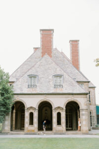 Glen Manor House Portsmouth RI | Deirdre Photography Timeless and Organic Moments | Historic stone building with three arched entrances and tall red chimneys. People stand under the arches on a serene, overcast day. Classic architecture vibe.