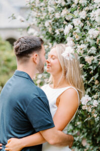 Glen Manor House Portsmouth RI | Deirdre Photography Timeless and Organic Moments | A couple embraces tenderly in a garden, surrounded by blooming white flowers. The scene exudes warmth and romance on a serene day.