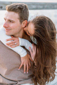 Blithewold Mansion, Gardens and Arboretum | Deirdre Photography Timeless and Organic Moments | A woman with long brown hair playfully embraces a man from behind. Both are smiling, creating a joyful and affectionate atmosphere.