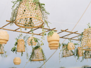 Lion Rock Farm Wedding | Deirdre Photography Timeless and Organic Moments | Hanging wicker lanterns adorned with greenery on bamboo poles, creating a rustic, organic ambiance against a soft, light blue sky.