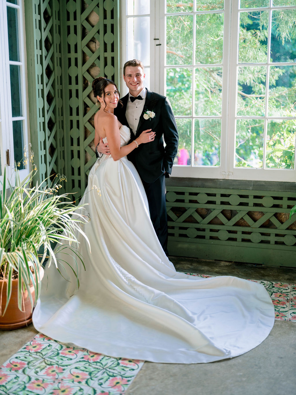The couple stands by tall windows with the bride’s gown sweeping across the patterned floor, a refined interior portrait by a Rhode Island wedding photographer.